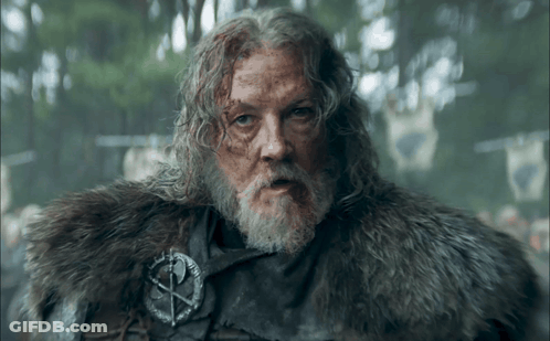 A Man With Long Hair And A Beard Is Wearing A Fur Coat And A Badge With A Cross On It GIF