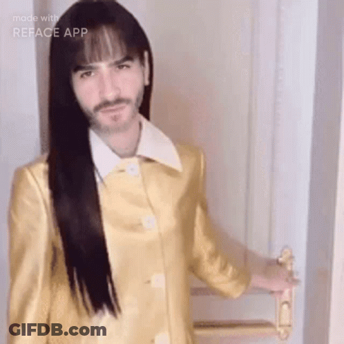 A Man With Long Hair And A Beard Is Wearing A Yellow Coat And Holding A Door Handle . GIF