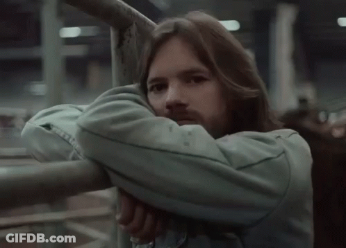 A Man With Long Hair And A Beard Leans Against A Metal Railing . GIF