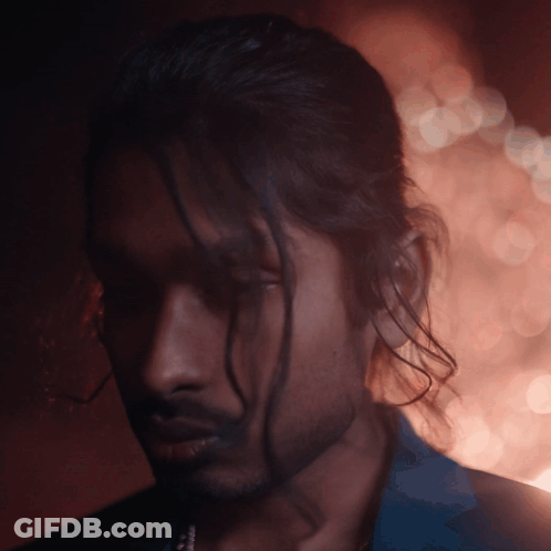 A Man With Long Hair And A Beard Looks Down At Something GIF