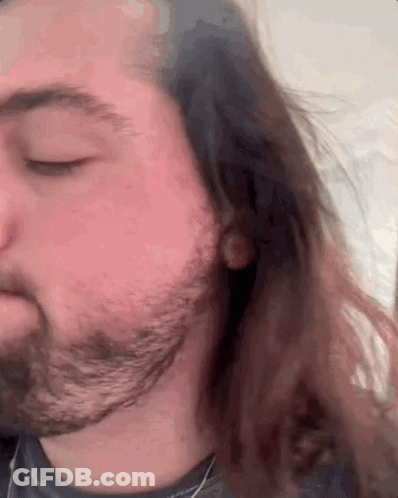 A Man With Long Hair And A Beard Looks Down With His Eyes Closed GIF