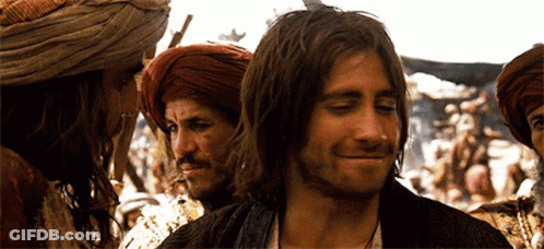 A Man With Long Hair And A Beard Smiles In Front Of A Group Of Men GIF