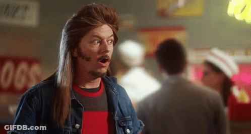 A Man With Long Hair And A Beard Stands In Front Of A Sign That Says Hot Dogs GIF