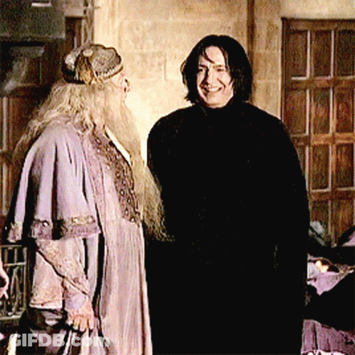 A Man With Long Hair And A Beard Stands Next To Another Man In A Black Coat GIF