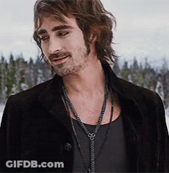 A Man With Long Hair And A Beard Wearing A Black Jacket And A Necklace . GIF