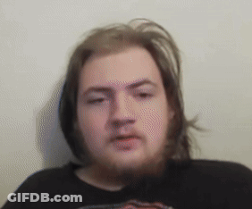 A Man With Long Hair And A Beard Wearing A Black Shirt Looks At The Camera GIF
