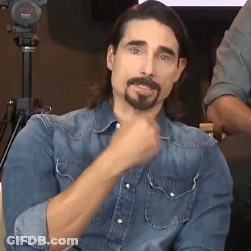 A Man With Long Hair And A Beard Wearing A Denim Shirt Is Making A Funny Face . GIF