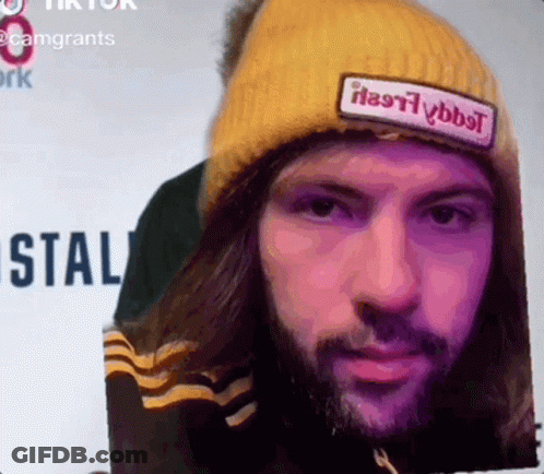 A Man With Long Hair And A Beard Wearing A Yellow Beanie With A Patch That Says " Heavyybbt " GIF