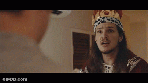 A Man With Long Hair And A Crown On His Head Is Talking To Another Person GIF