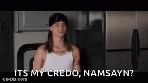 A Man With Long Hair And A Hat Is Sitting In Front Of A Refrigerator And Talking . GIF