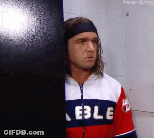 A Man With Long Hair And A Headband Is Leaning Against A Wall In A Room . GIF