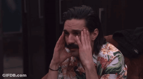 A Man With Long Hair And A Mustache Holds His Head GIF
