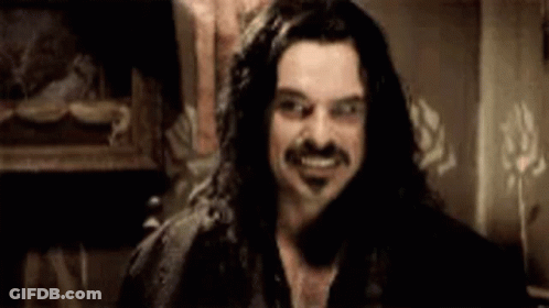 A Man With Long Hair And A Mustache Is Smiling And Looking At The Camera . GIF