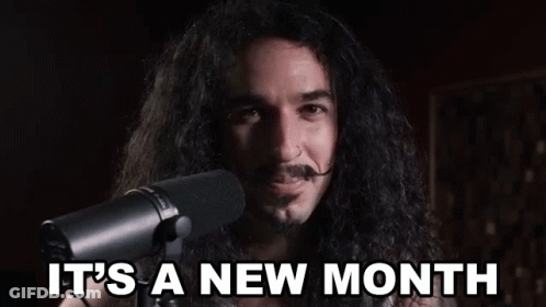 A Man With Long Hair And A Mustache Is Standing In Front Of A Microphone And Saying `` It 'S A New Month '' GIF
