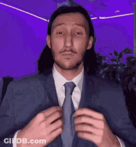 A Man With Long Hair And A Mustache Is Tying His Tie . GIF