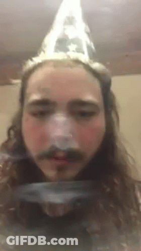 A Man With Long Hair And A Mustache Is Wearing A Cone Hat . GIF