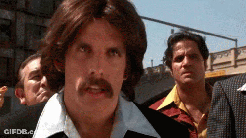 A Man With Long Hair And A Mustache Stands In Front Of A Group Of Men GIF