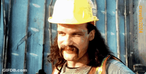 A Man With Long Hair And A Mustache Wearing A Hard Hat With The Year 2004 On The Bottom Right GIF