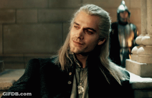 A Man With Long Hair And A Necklace With A Lion On It Smiles GIF