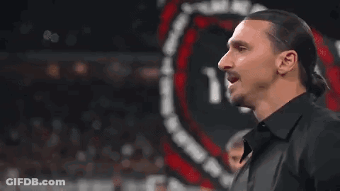 A Man With Long Hair And A Ponytail Is Standing In Front Of A Sign . GIF