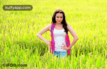 A Man With Long Hair And A Red Shirt Is Smiling In A Field . GIF