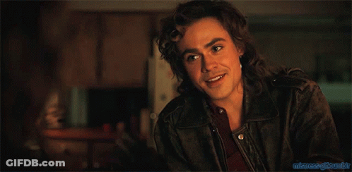 A Man With Long Hair And A Ring On His Finger Is Sitting At A Table In A Dark Room GIF