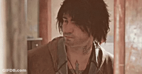A Man With Long Hair And A Tattoo On His Neck Is Standing In A Room . GIF