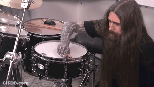 A Man With Long Hair And A Tattooed Arm Playing A Drum Set GIF