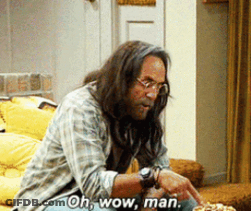 A Man With Long Hair And Glasses Is Sitting On A Couch And Says Oh Wow Man GIF