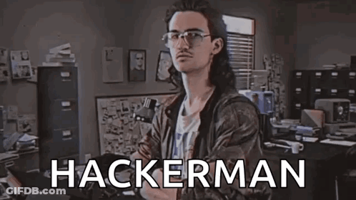 A Man With Long Hair And Glasses Is Standing In A Room With The Word Hackerman Written On The Screen . GIF