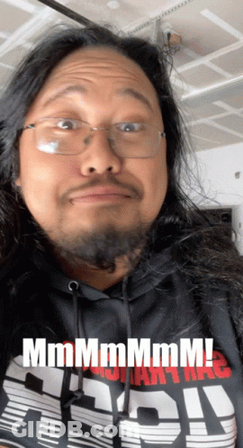 A Man With Long Hair And Glasses Is Wearing A Shirt That Says " Mmmmm " GIF