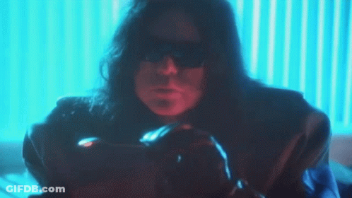 A Man With Long Hair And Sunglasses Is Sitting In Front Of A Blue Wall GIF