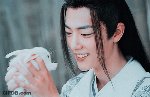 A Man With Long Hair Holds A Small White Rabbit In His Hands GIF