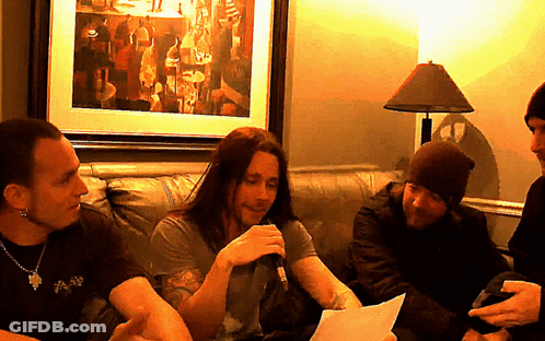 A Man With Long Hair Is Holding A Microphone And Talking To Another Man GIF