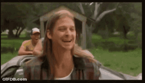 A Man With Long Hair Is Laughing While Sitting In A Car With Another Man . GIF