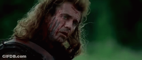 A Man With Long Hair Is Laying In The Grass With Blood On His Face . GIF