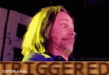 A Man With Long Hair Is Making A Funny Face In Front Of A Sign That Says Triggered GIF