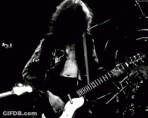 A Man With Long Hair Is Playing A Guitar In A Black And White Photo . GIF
