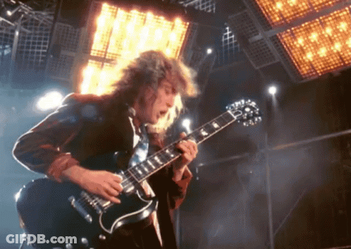 A Man With Long Hair Is Playing A Guitar In Front Of A Large Light GIF