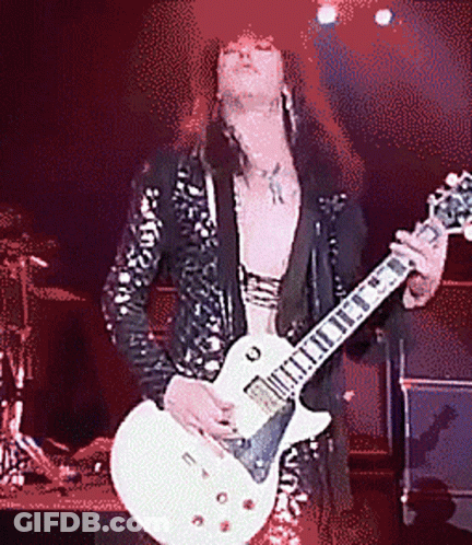 A Man With Long Hair Is Playing A Guitar On A Stage GIF