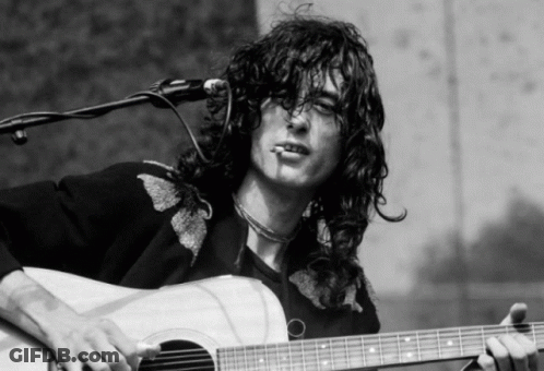 A Man With Long Hair Is Playing An Acoustic Guitar And Smoking A Cigarette GIF