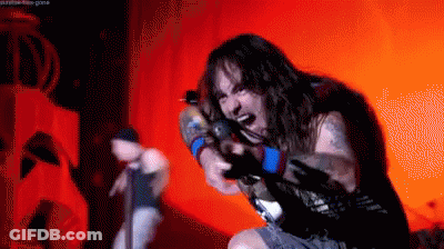 A Man With Long Hair Is Singing Into A Microphone In A Dark Room GIF