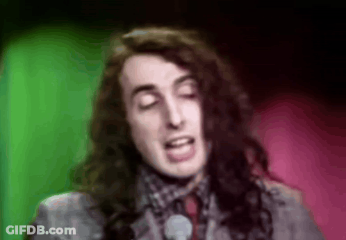 A Man With Long Hair Is Singing Into A Microphone In Front Of A Green And Pink Background . GIF