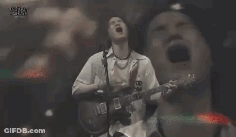A Man With Long Hair Is Singing Into A Microphone While Making A Funny Face . GIF