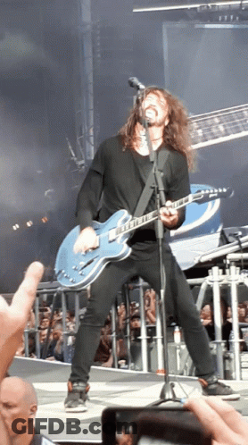 A Man With Long Hair Is Singing Into A Microphone While Playing A Guitar GIF