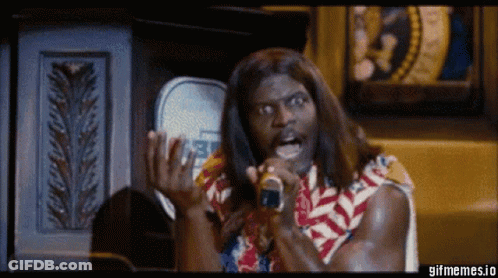 A Man With Long Hair Is Singing Into A Microphone While Wearing A Colorful Shirt . GIF