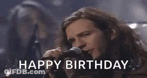 A Man With Long Hair Is Singing Into A Microphone With The Words `` Happy Birthday '' . GIF