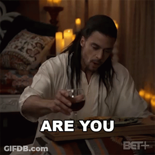 A Man With Long Hair Is Sitting At A Table With A Glass Of Wine And Says " Are You " GIF