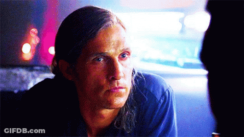 A Man With Long Hair Is Sitting In A Dark Room Looking At Something GIF