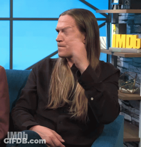 A Man With Long Hair Is Sitting In Front Of A Sign That Says Imdb On It GIF